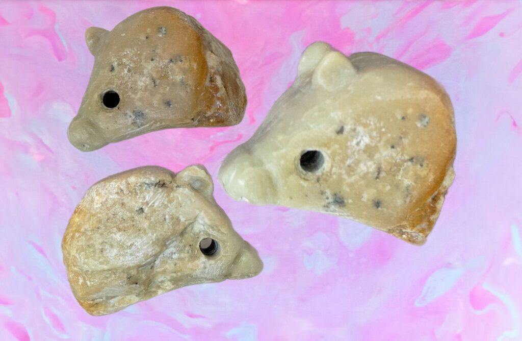 Drei helle steinähnliche Figuren in Tierform mit schwarzen Punkten auf rosa Hintergrund