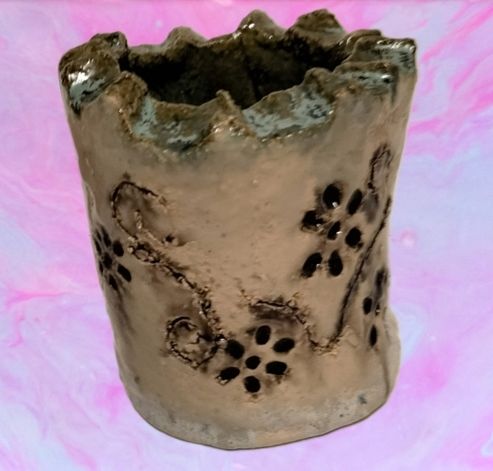 Ein grauer, unregelmäßig geformter Keramikbecher mit Blumenmotiv vor rosa Hintergrund