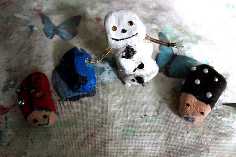 Ein selbstgebastelter Schneemann lächelt freundlich neben drei bunt bemalten Steinen