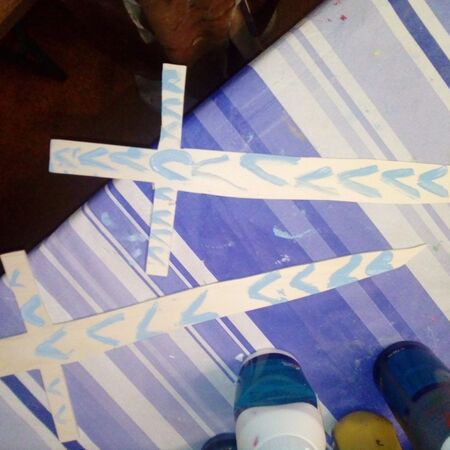 Zwei aus Papier gebastelte Schwerter mit blauem Muster liegen auf einer gestreiften Tischdecke