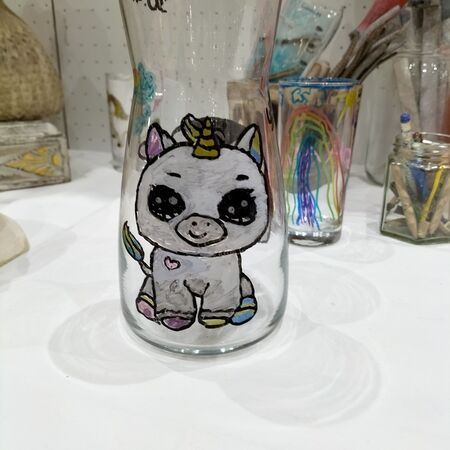 Ein Glas mit einem bunten, lächelnden Einhorn mit großen Augen und Herzdeko