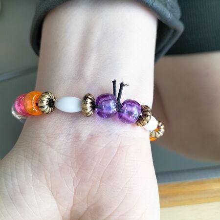 Ein Arm mit einem bunten Perlenarmband, lila und orange Perlen stechen hervor