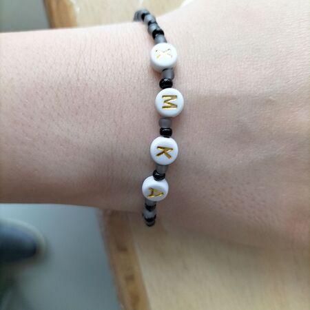 Eine helle Hand trägt ein Perlenarmband mit den Buchstaben K M X in Gelb