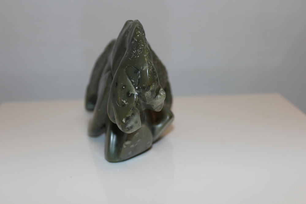 Eine grüne Steinskulptur mit glatter Oberfläche steht auf einem weißen Untergrund