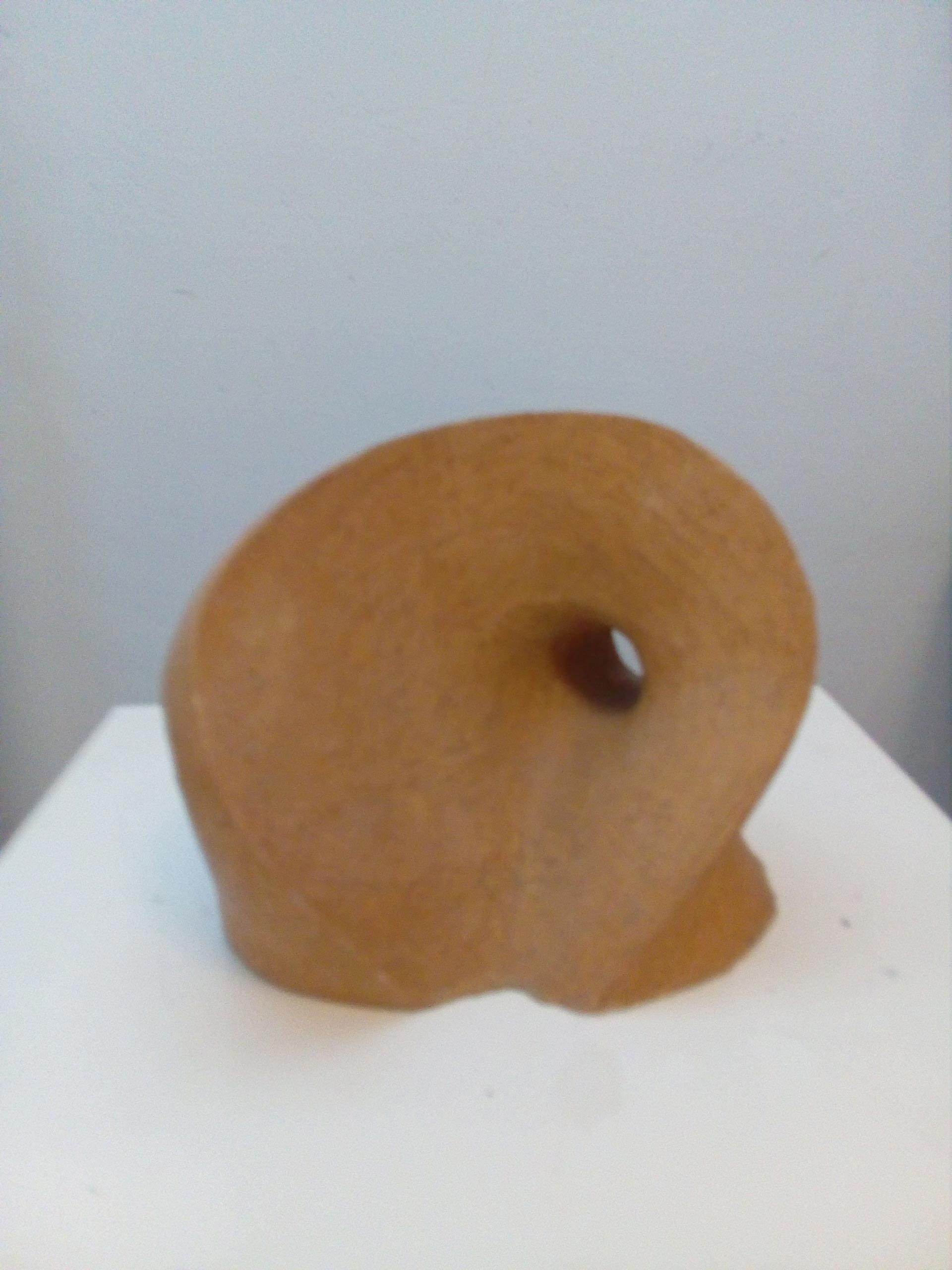 Eine abstrakte braune Skulptur mit rundem Loch in der Mitte auf weißem Sockel