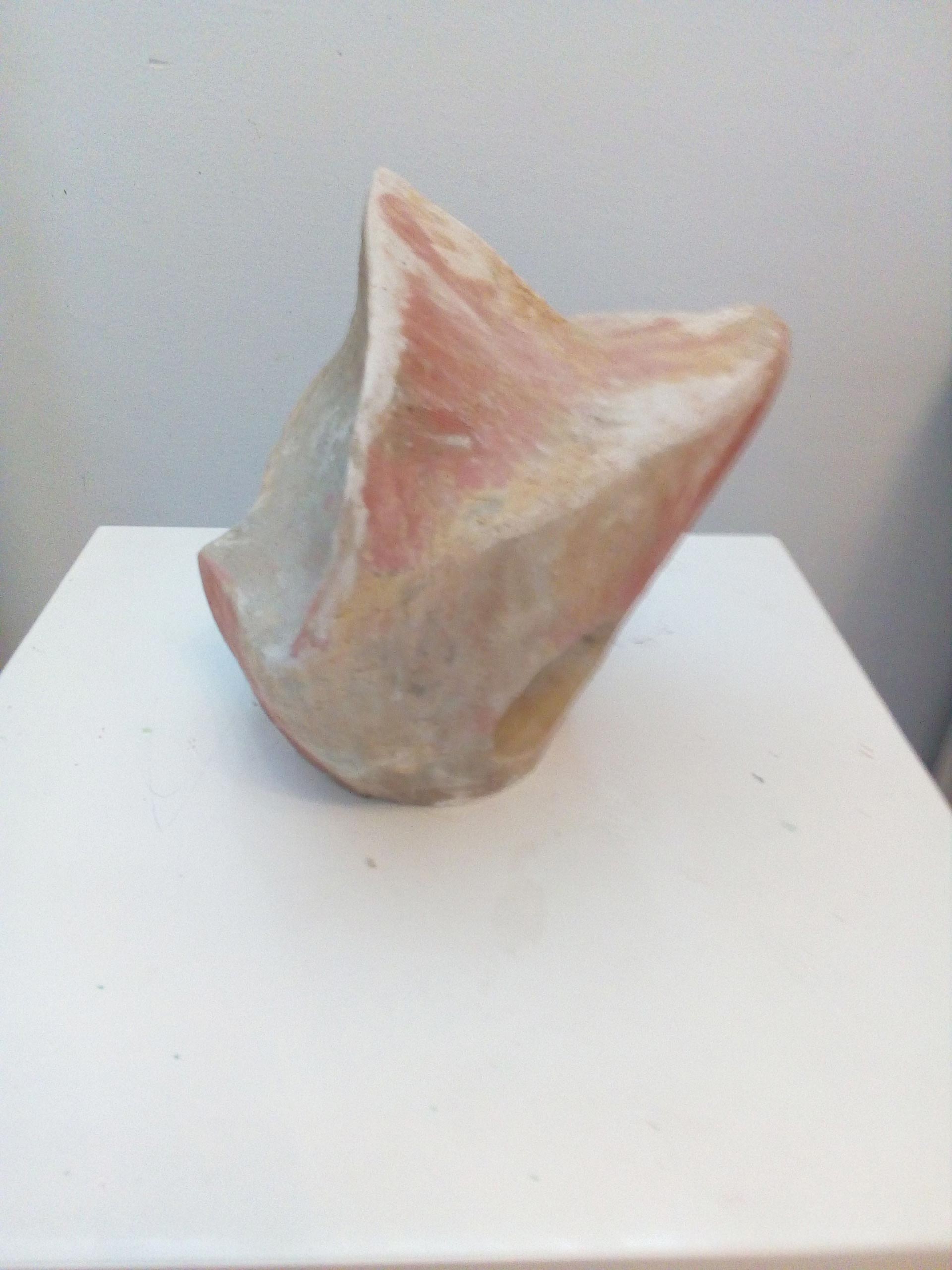 Abstrakte Skulptur mit rauer Oberfläche in Rosa und Beige auf weißem Podest