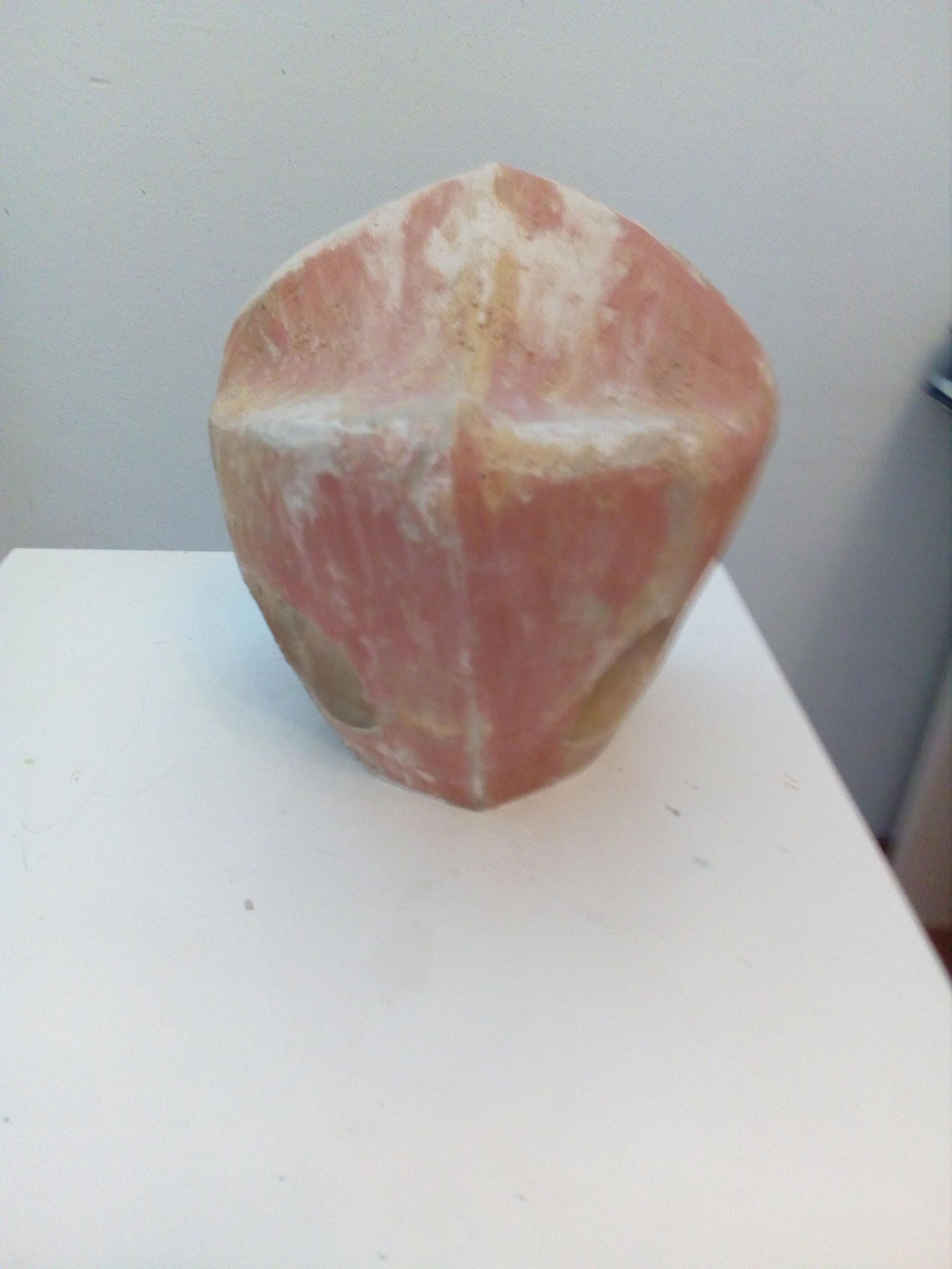 Eine rosafarbene, kopfförmige Skulptur mit kantigen Zügen und großen Augenöffnungen