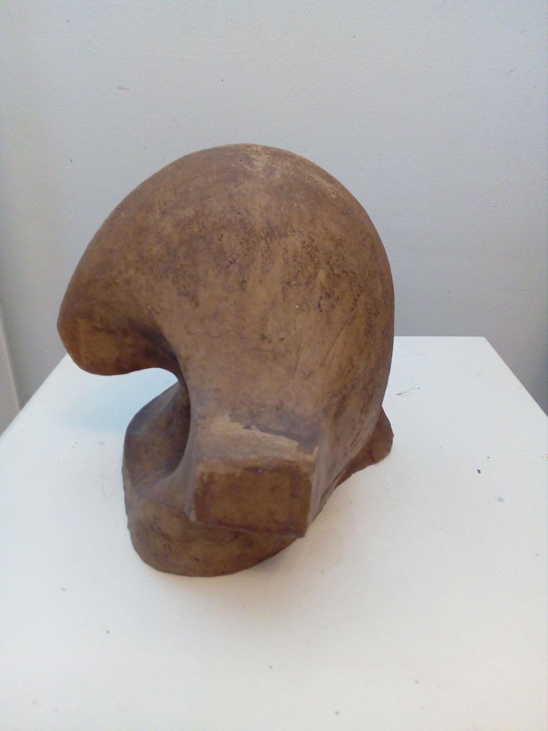 Eine abstrakte braune Skulptur mit glatter Oberfläche und ungewöhnlicher Rundung steht auf einem weißen Podest