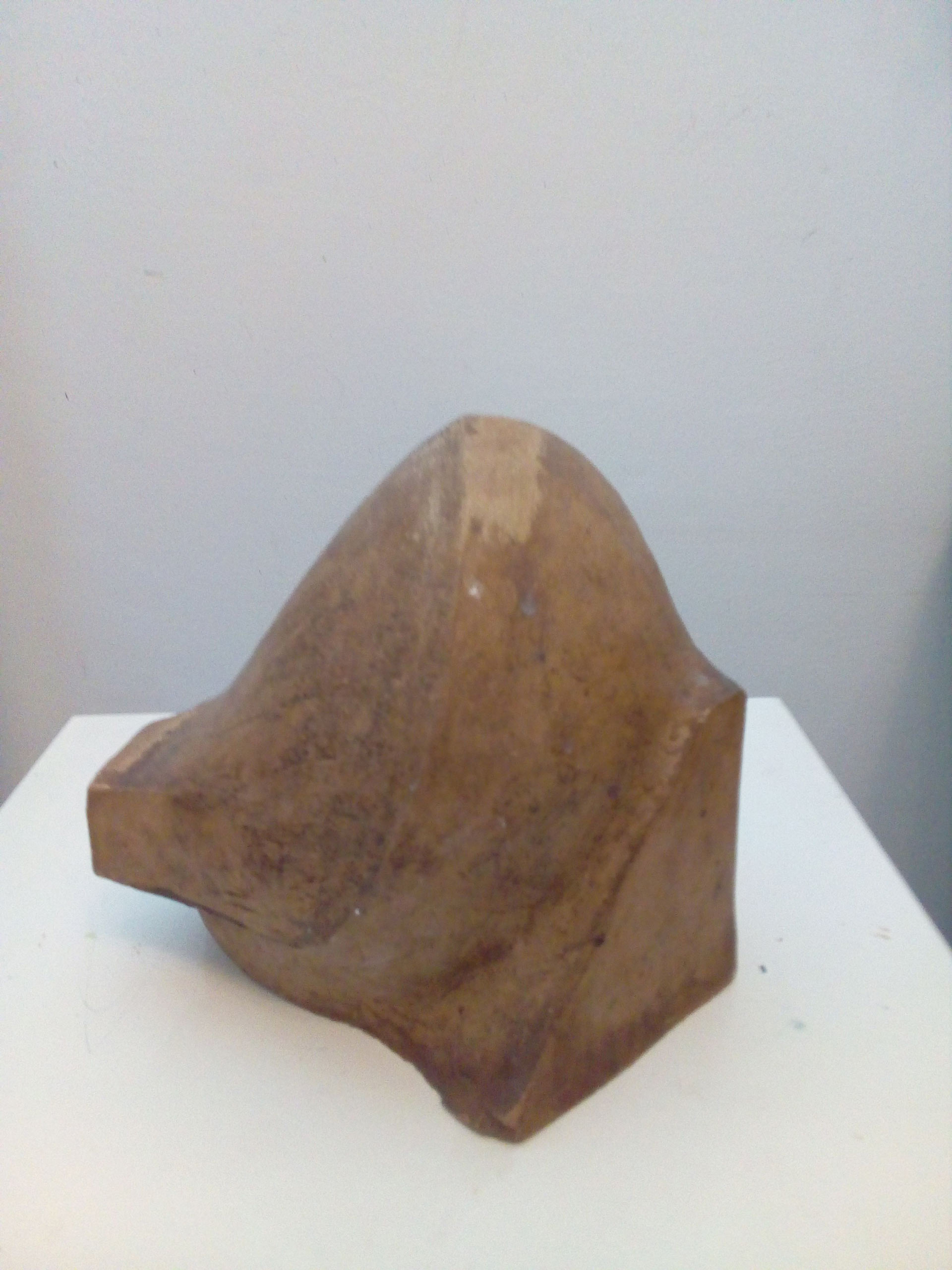 Eine abstrakte braune Skulptur mit glatten und kantigen Flächen auf weißem Sockel