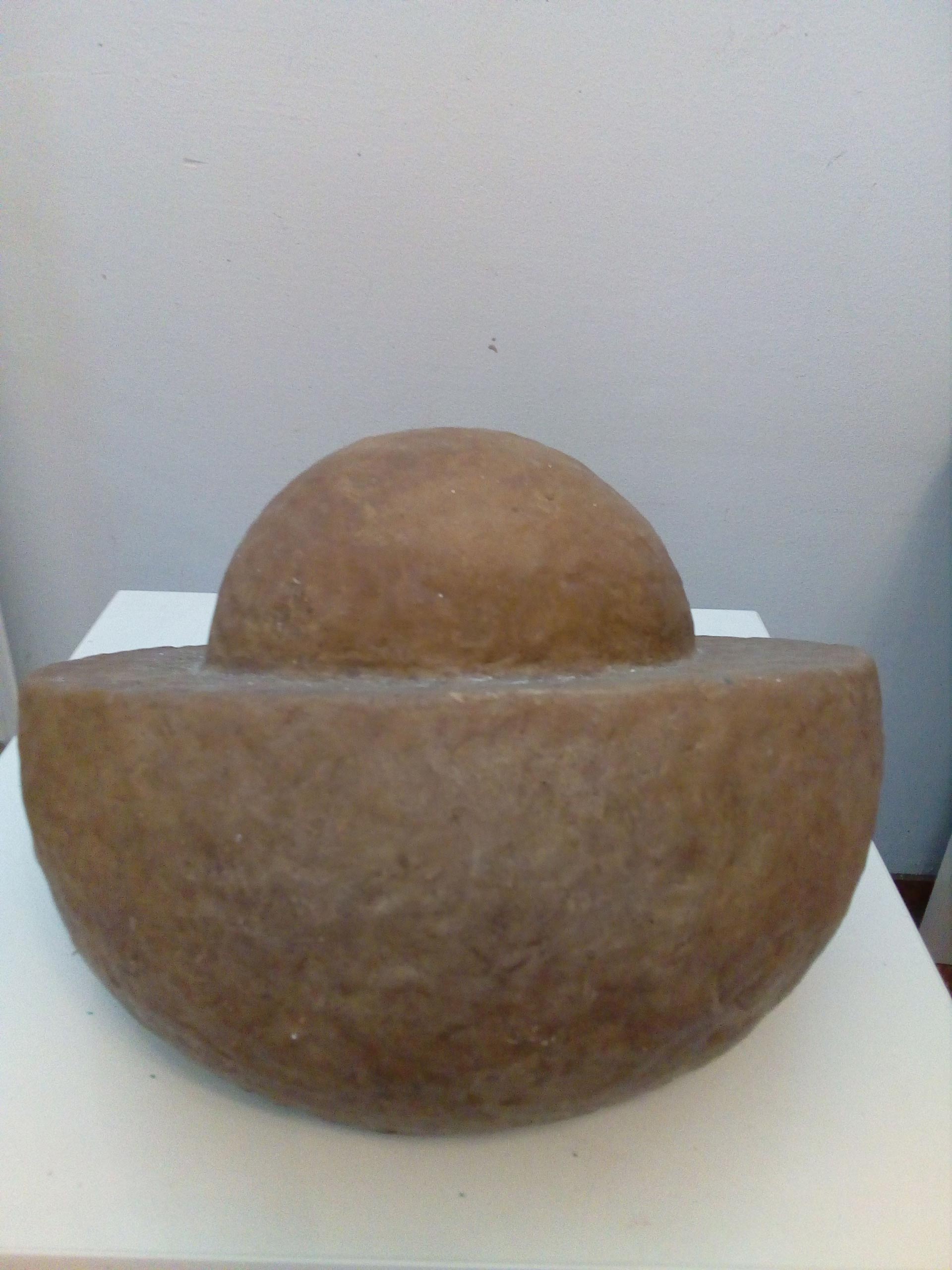 Eine braune Skulptur mit halbrunder Form steht auf einem weißen Podest