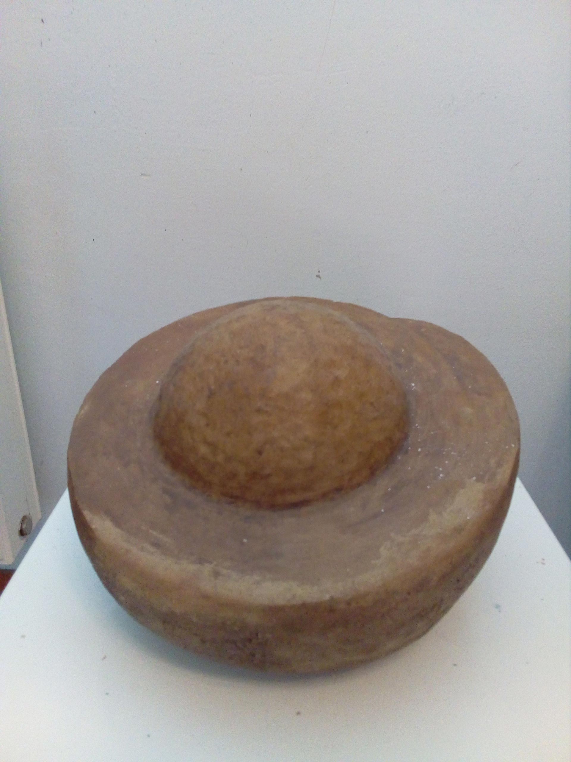Ein braunes, rundes Objekt mit einer Kuppel in der Mitte steht auf einem weißen Tisch