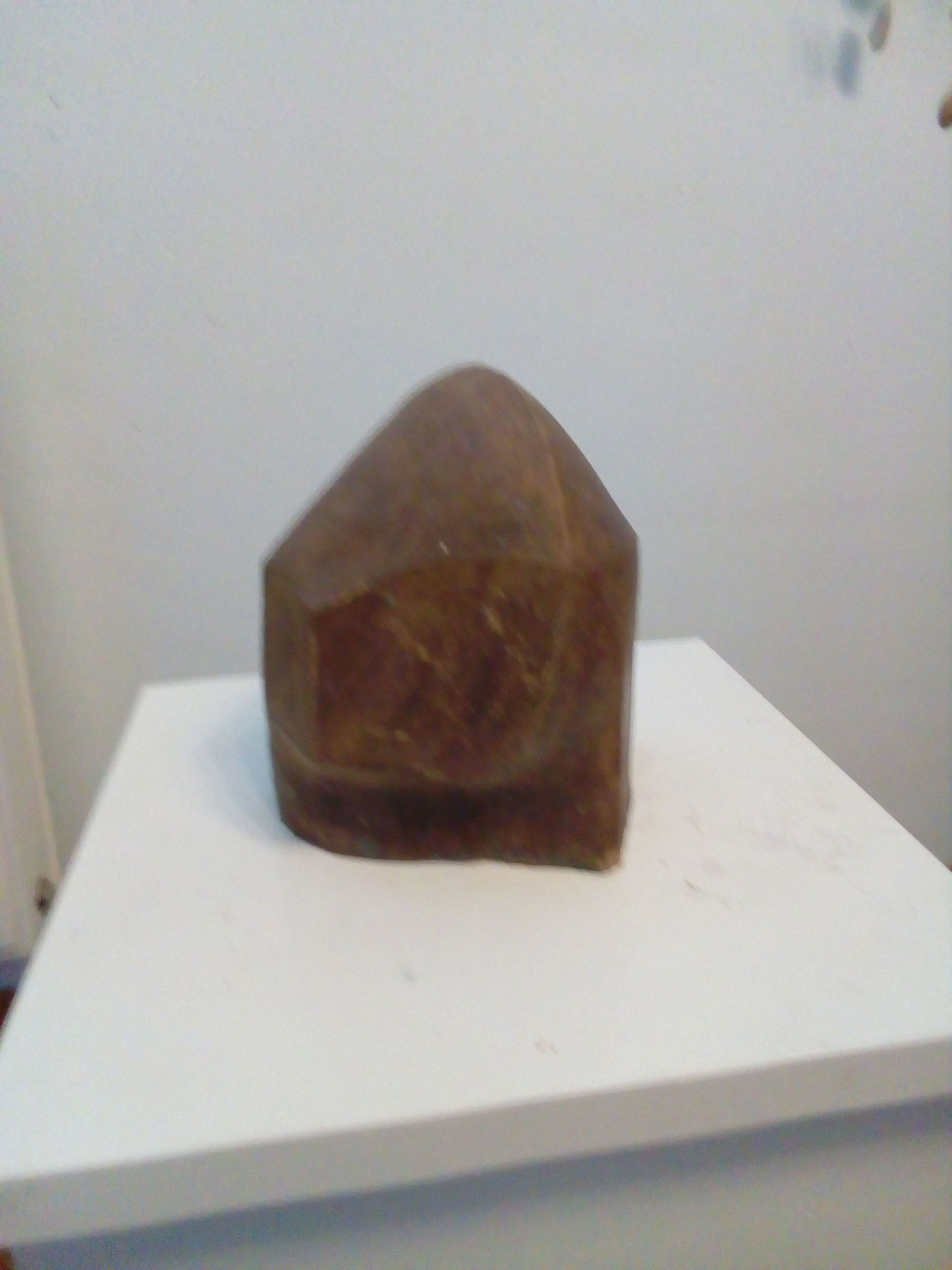 Eine braune, abstrakte Skulptur mit klaren Kanten steht auf einem weißen Sockel