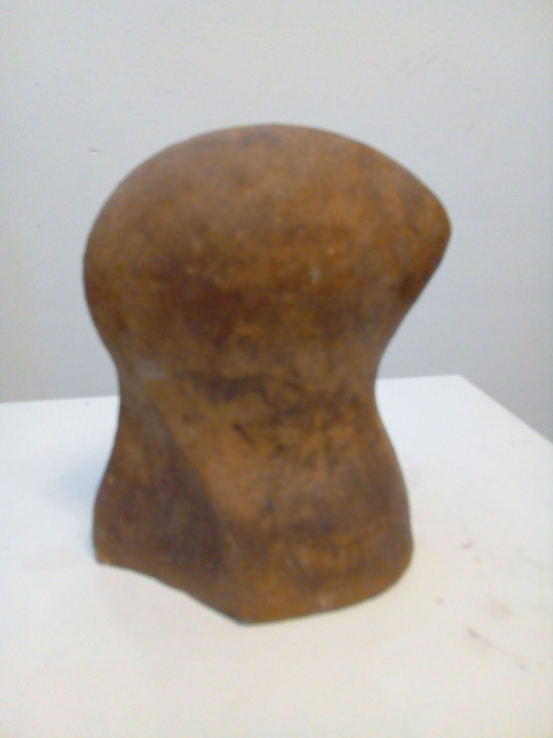 Eine braune Skulptur mit runder Oberseite steht auf einer weißen Fläche