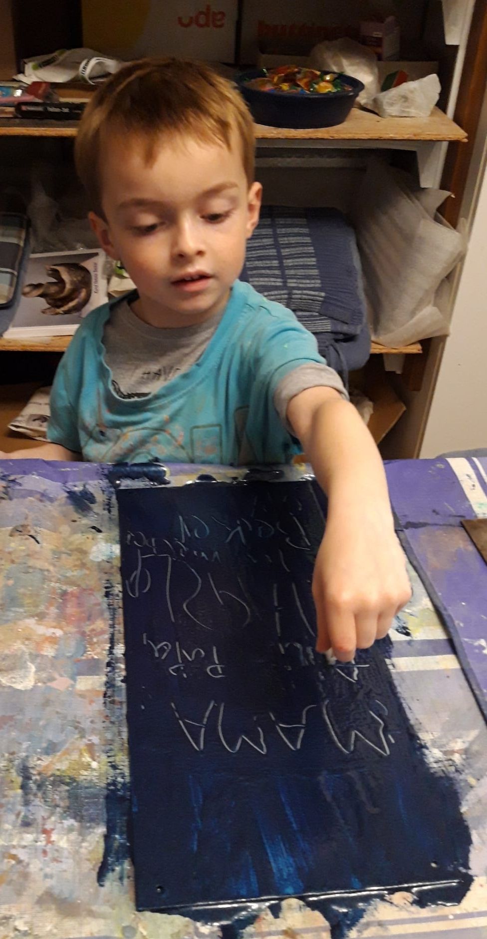 Ein kleiner Junge mit konzentriertem Blick malt mit weißer Kreide auf dunkelblauem Papier