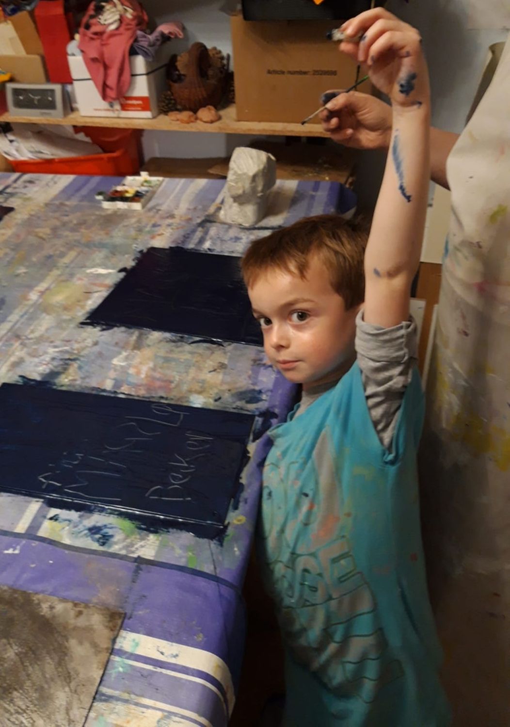 Ein Junge mit neugierigem Blick hebt den Arm, seine Hand und sein Arm sind blau bemalt