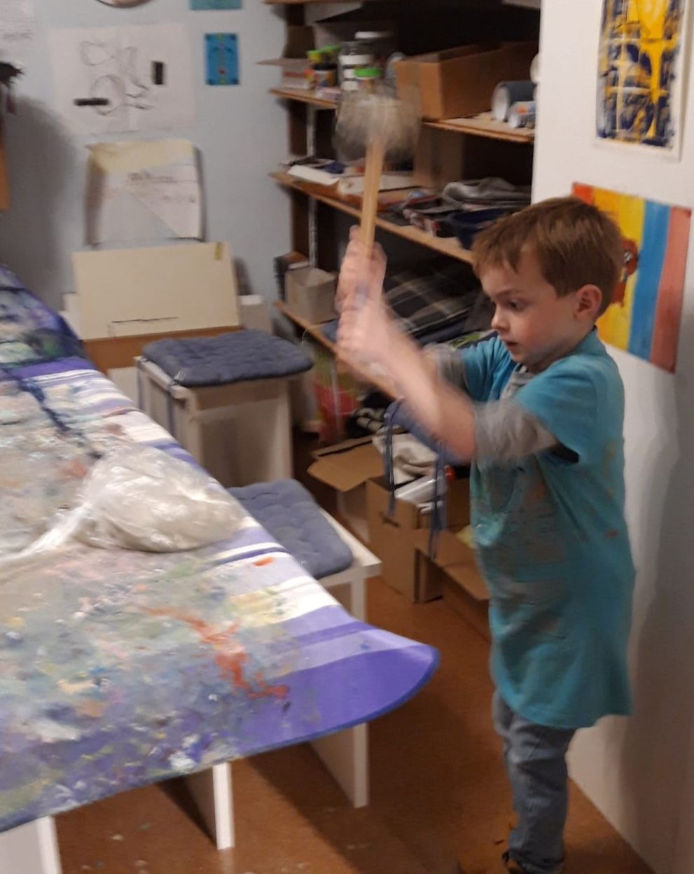 Ein konzentrierter Junge schlägt mit einem Hammer auf einen Plastiksack auf einem bunten Tisch