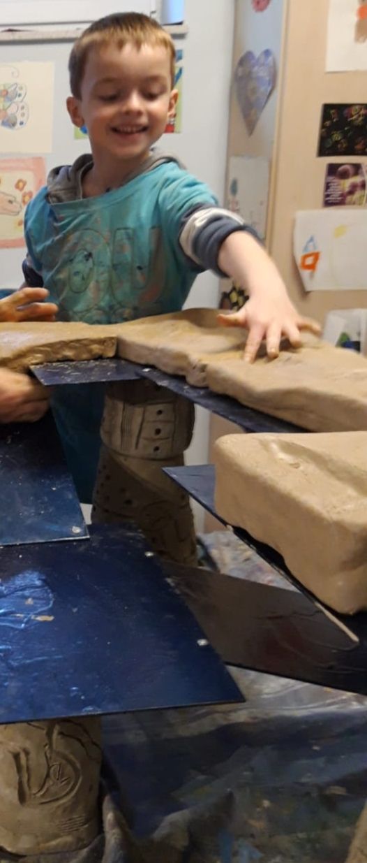 Ein fröhlicher Junge im blauen Pullover berührt lachend große sandfarbene Steine