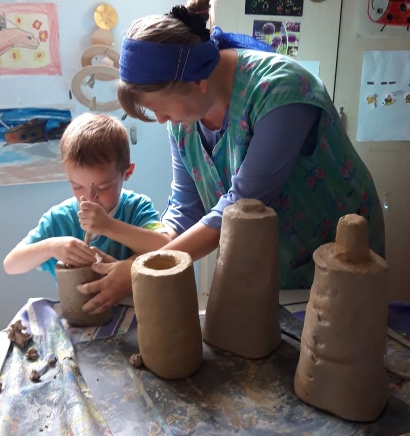 Eine Frau hilft einem Jungen konzentriert beim Töpfern mit feuchtem braunem Ton