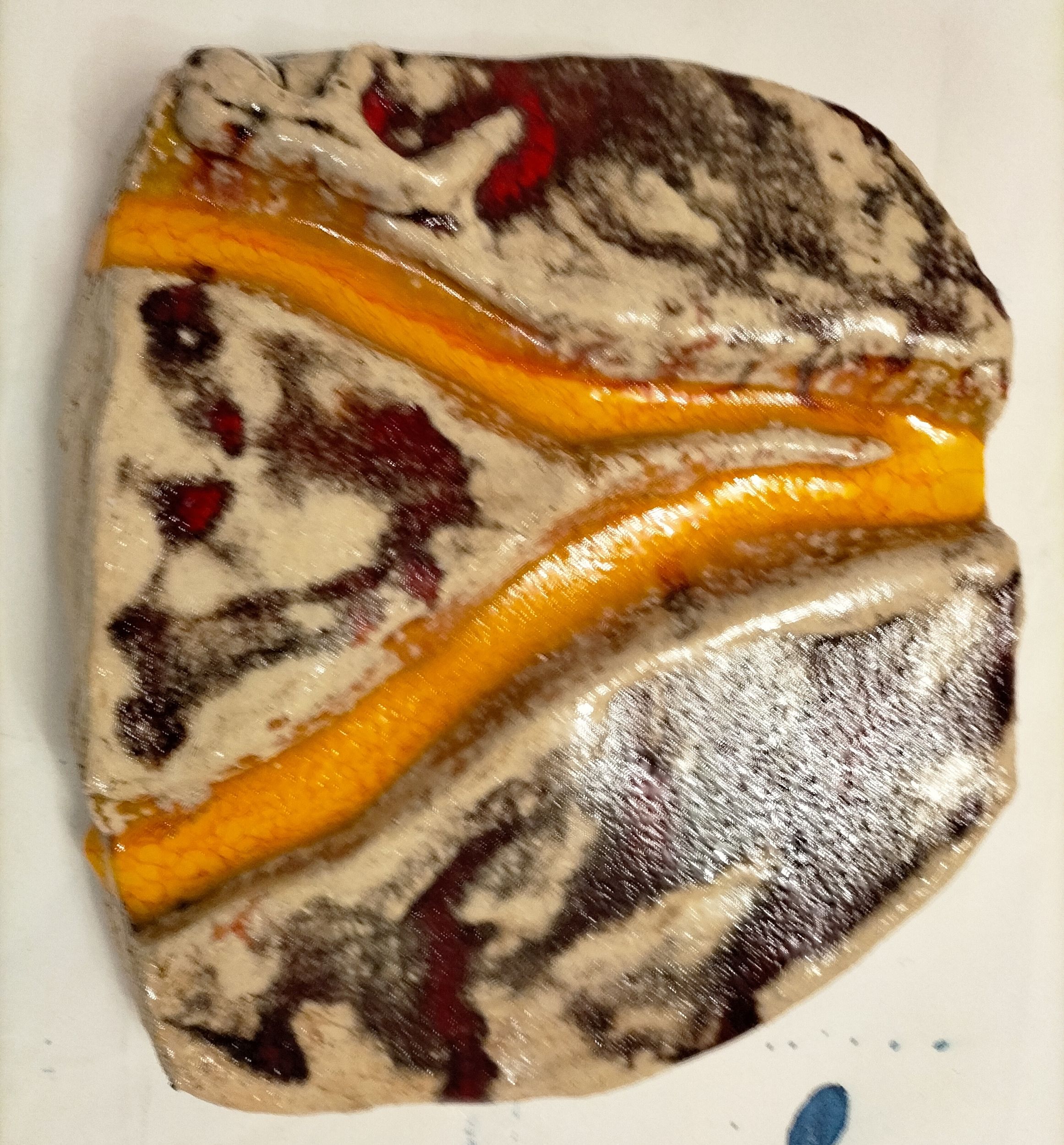 Ein flacher Stein mit orangefarbenen und schwarzen Linien und cremefarbenen Mustern