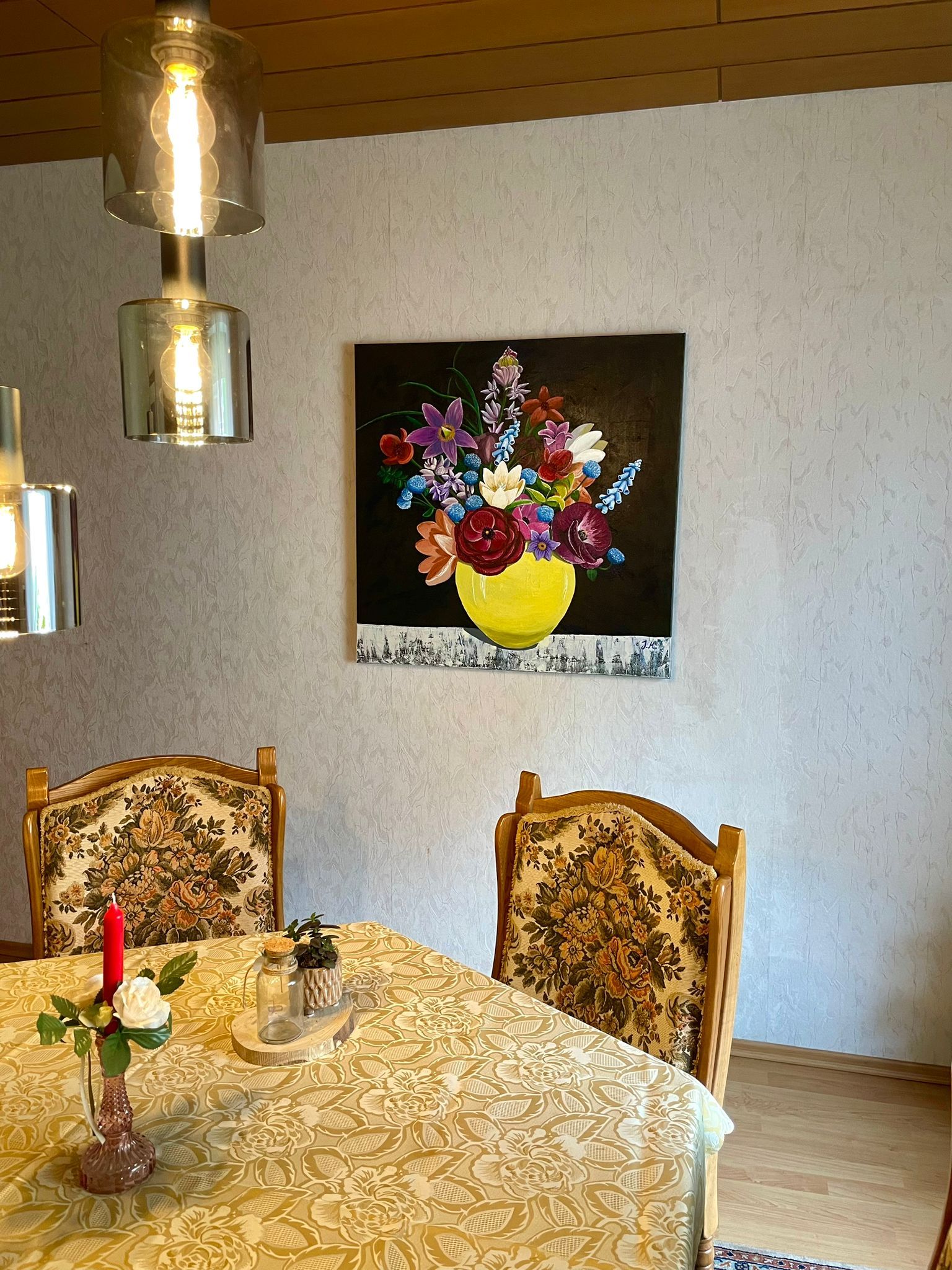 Ein Esszimmer mit floralen Polsterstühlen, gelber Tischdecke und Blumenbild an der Wand