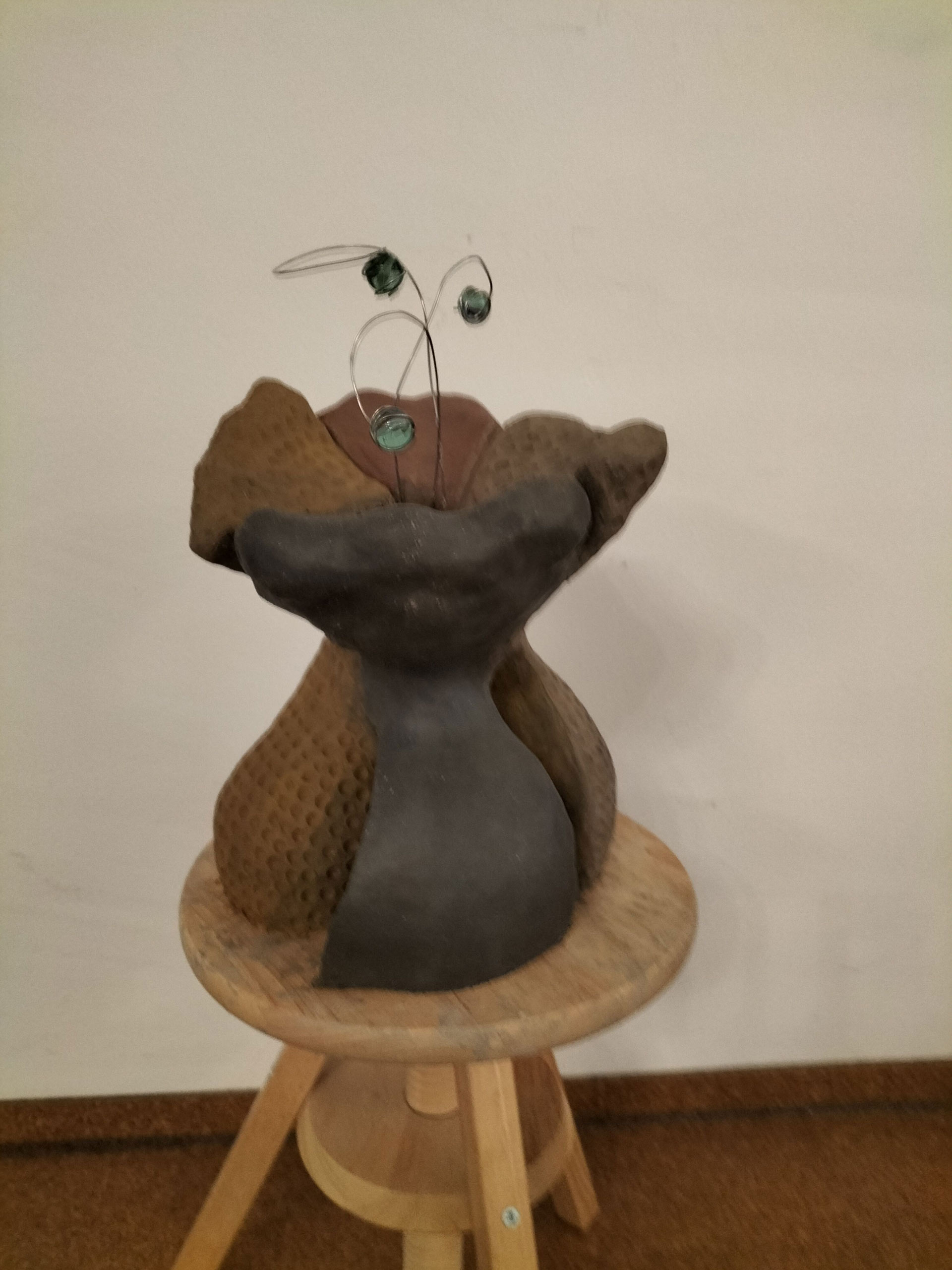 Keramikskulptur in Erdtönen auf Hocker mit abstrakten Formen und grünen Drahtdetails