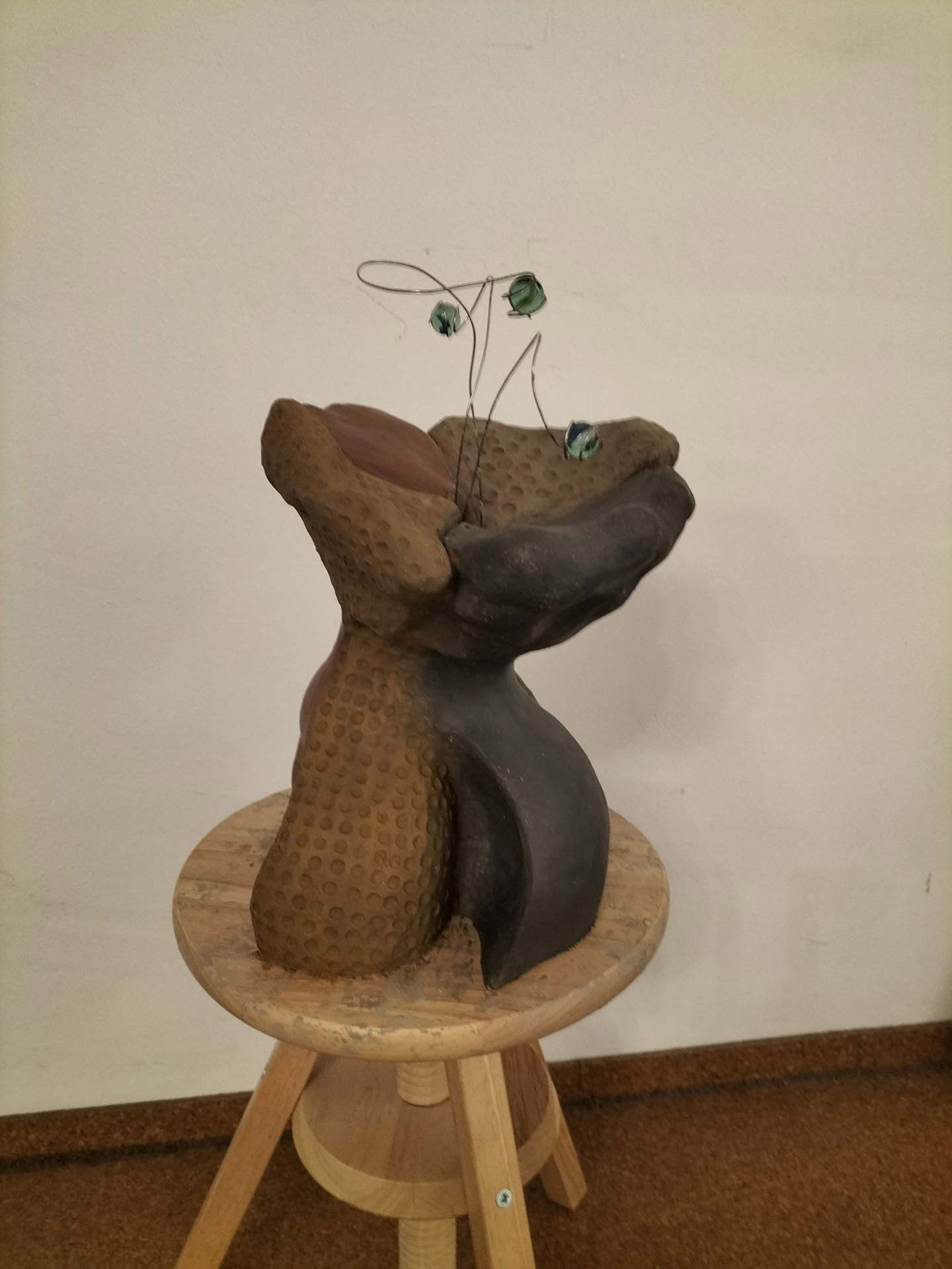 Eine braune abstrakte Skulptur mit runden Mustern und Drahtstielen mit grünen Blättern