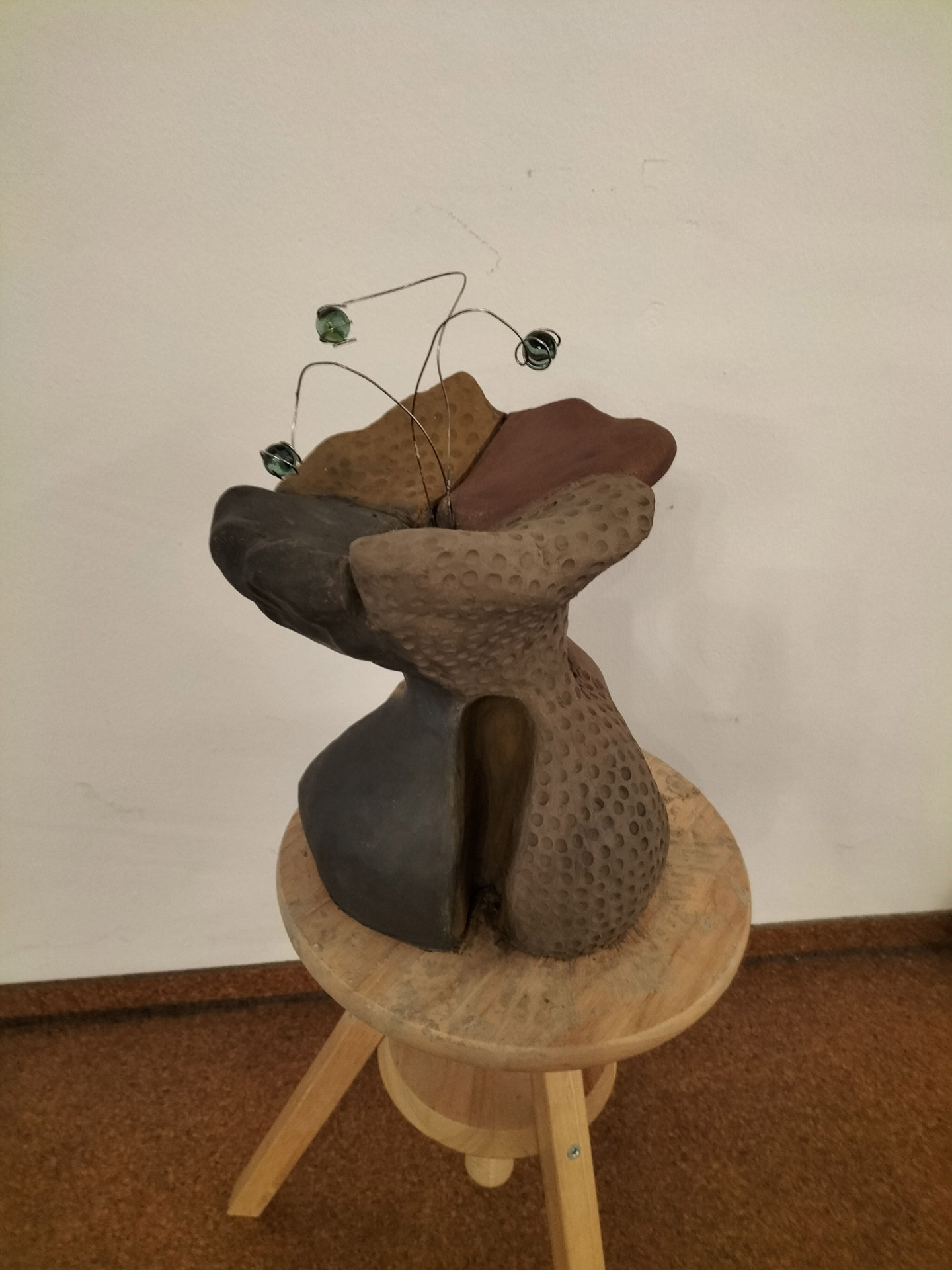 Abstrakte Skulptur aus braunem und grauem Ton mit strukturierten Flächen auf einem Hocker