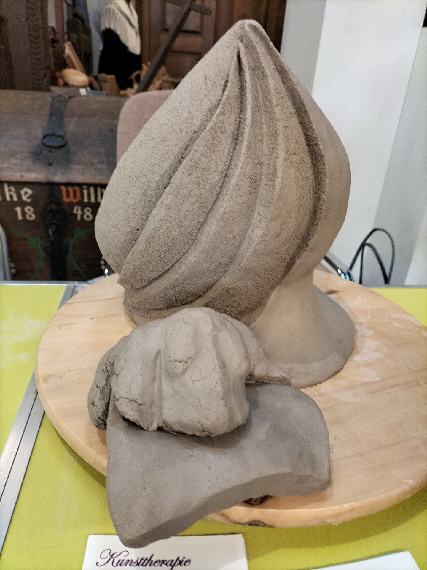 Eine graue Tonfigur mit geschwungenen Linien steht neben einer unfertigen Skulptur