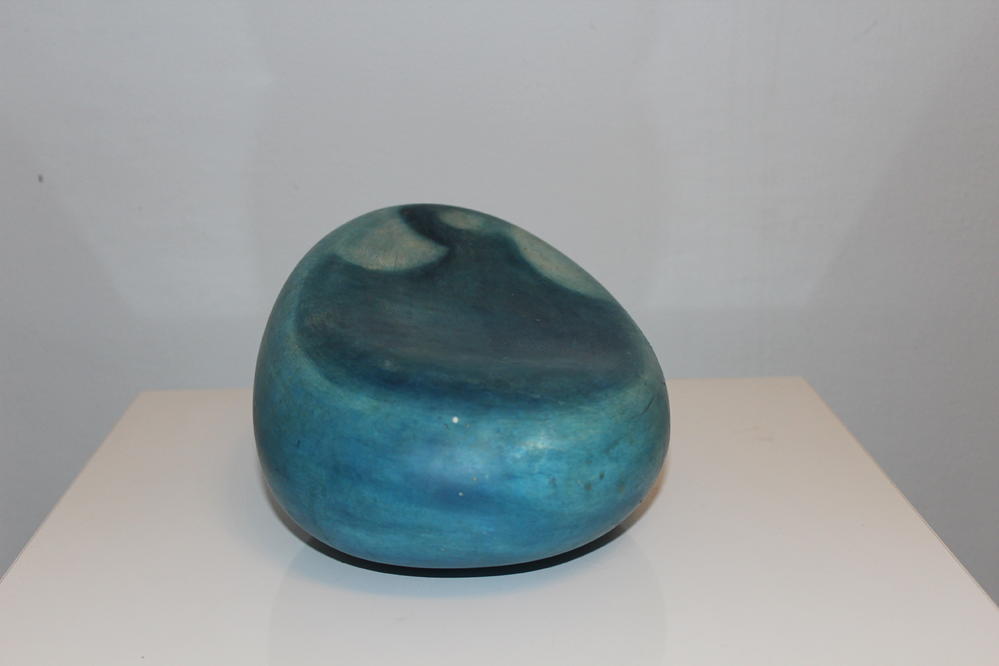Ein glatter, blauer Stein mit mattem Glanz liegt auf einer weißen Oberfläche