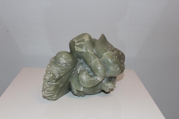 Eine grüne abstrakte Steinskulptur mit geschwungenen Formen steht auf einem weißen Podest