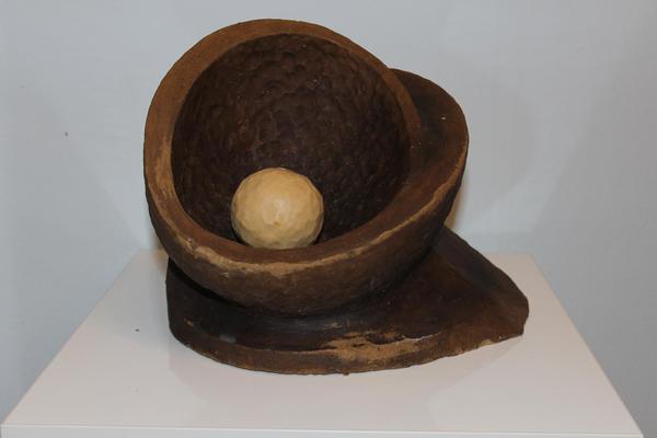 Eine abstrakte braune Skulptur mit rundem Hohlraum und einer beigefarbenen Kugel innen
