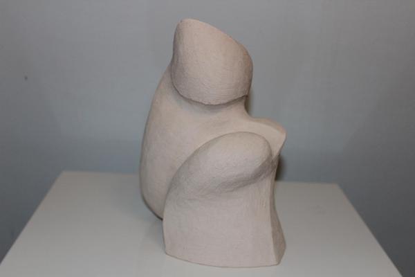 Eine cremefarbene abstrakte Skulptur steht auf einem weißen Podest und wirkt harmonisch