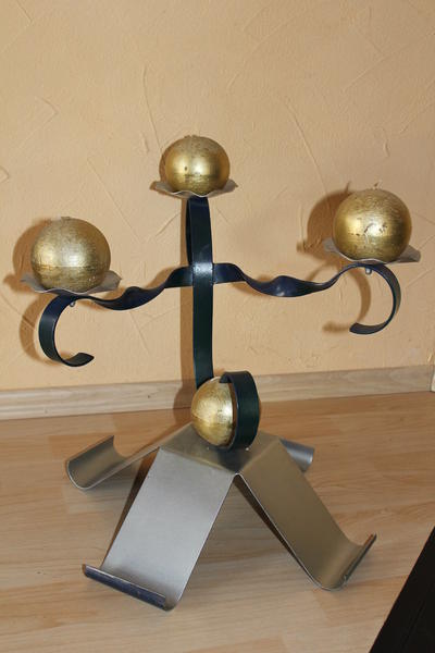 Ein kunstvoller silberner Kerzenhalter mit drei goldenen Kugeln auf Holzfußboden