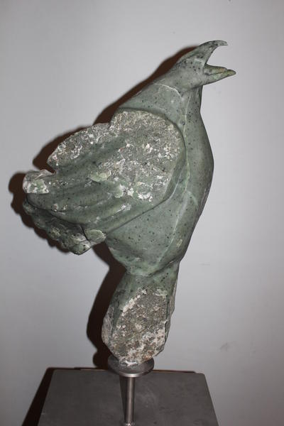 Eine grünliche Steinskulptur eines ausdrucksstark rufenden Vogels mit rauer Oberfläche