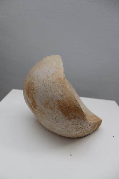 Eine beige-braune abstrakte Skulptur mit glatter Oberfläche steht auf einem weißen Sockel