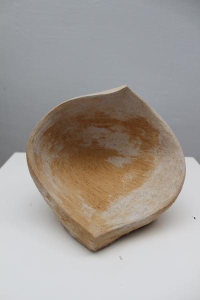Eine asymmetrische, cremefarbene Tonschale mit rauer Textur auf weißem Podest