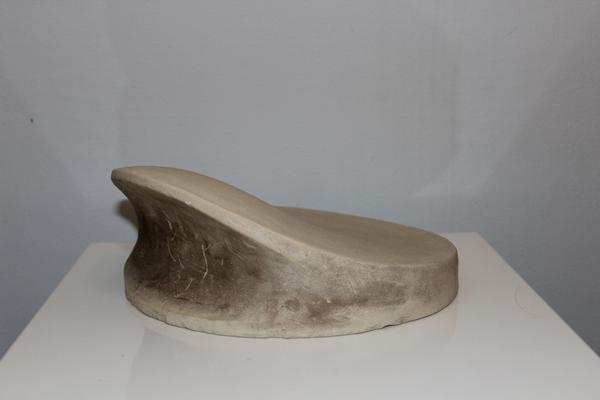 Eine abstrakte, beige Skulptur mit sanft geschwungener Form auf weißem Sockel
