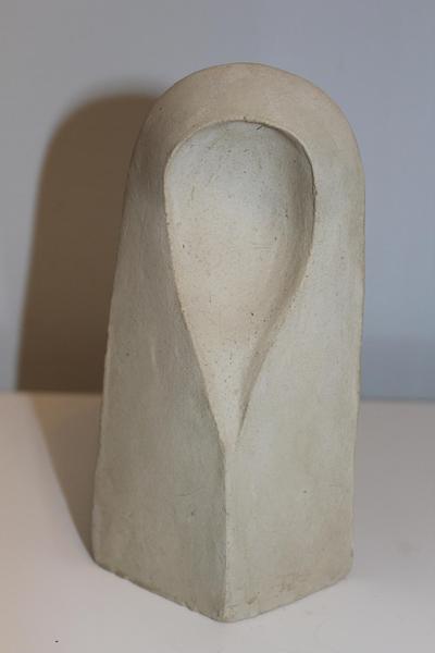 Eine beige Skulptur mit glatter Oberfläche und abstrakter Kopfform steht aufrecht
