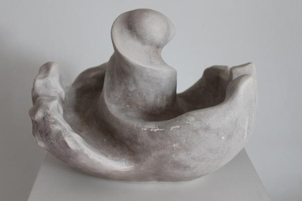 Eine abstrakte graue Skulptur mit glatten und gewellten Oberflächen steht auf einem Podest