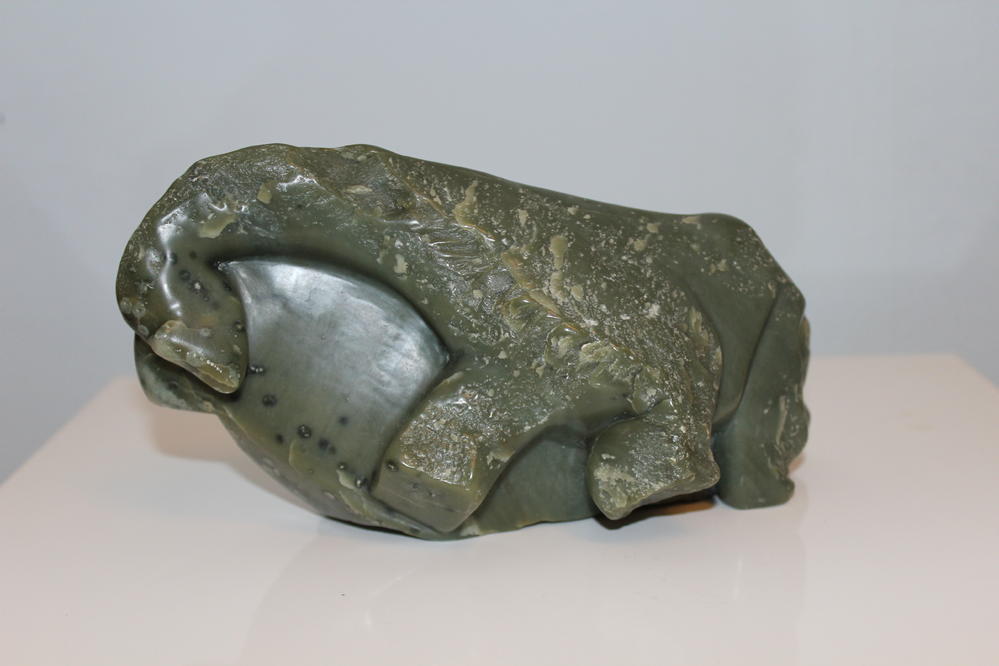Grüne Steinskulptur eines liegenden Tieres mit glatter Oberfläche und Musterung