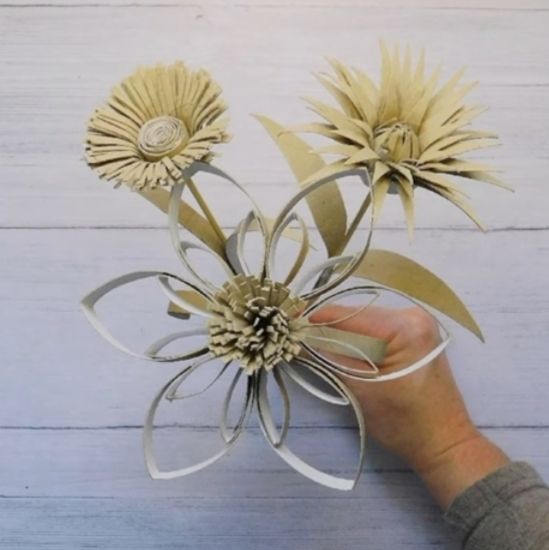 Hand haelt graues Papierblumenbuendel mit filigranen Blueten auf Holzgrund