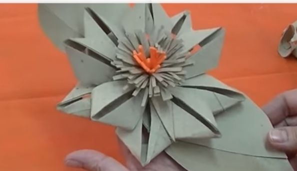 Haende halten graue Papierblume mit orangener Mitte, neutraler Ausdruck