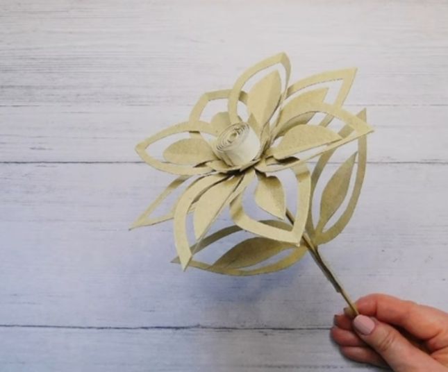 Hand haelt goldene Papierblume mit ruhigem Griff und zarten Blaettern