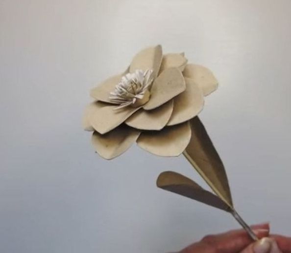 Hand haelt beige Papierblume mit weisser Mitte und gebogenen Blaettern