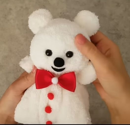 Haende halten weissen Teddybear mit Laecheln und roter Schleife