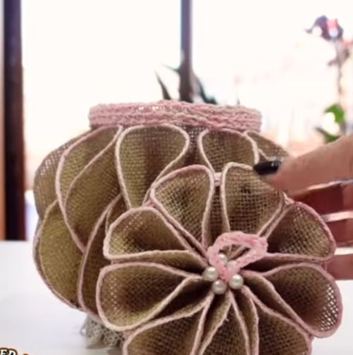 Hand mit schwarzem Nagellack hält braune Stoffblume mit Perlen