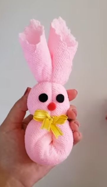 Hand haelt rosa Sockenhase mit frohem Blick und gelber Schleife