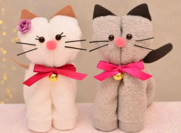 Zwei lächelnde Stoffkatzen in Weiß und Grau mit rosa Schleifen und Glöckchen