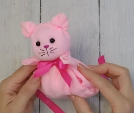 Sie halten eine rosa Stoffmaus mit freundlichem Gesicht und Schleife