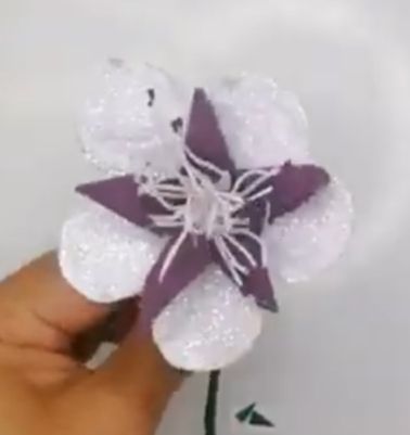 Hand haelt violette und weisse Glitzerblume mit drahtigem Stiel und Staubfaeden